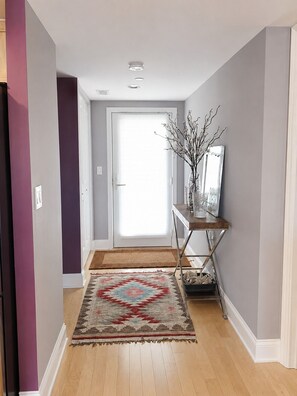 A hallway with a patterned rug, a console table with a vase, and a door with a view to the outside.