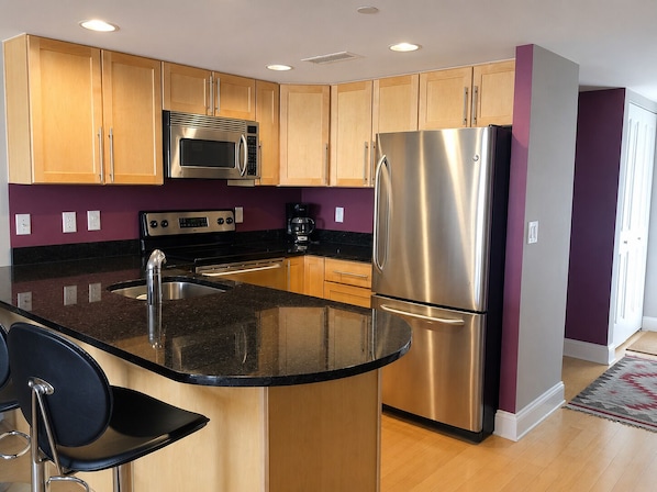 A modern kitchen with stainless steel appliances, wooden cabinets, and a black countertop.