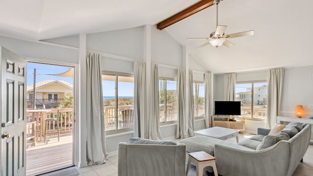 Een ruime woonkamer met een grote bank, een salontafel en een flatscreen-tv. Er is een balkon met uitzicht op zee en gebouwen.
