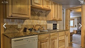 A kitchen with wooden cabinets, a granite countertop, a dishwasher, a microwave, and a stone backsplash.