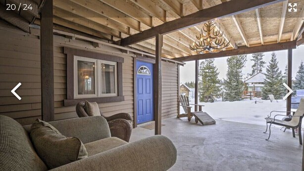 A covered porch with a blue door, wooden benches, and a view of a snowy landscape.