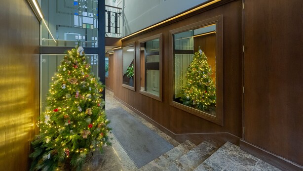 Un pasillo de hotel con dos árboles de Navidad, una escalera y ventanas amplias.