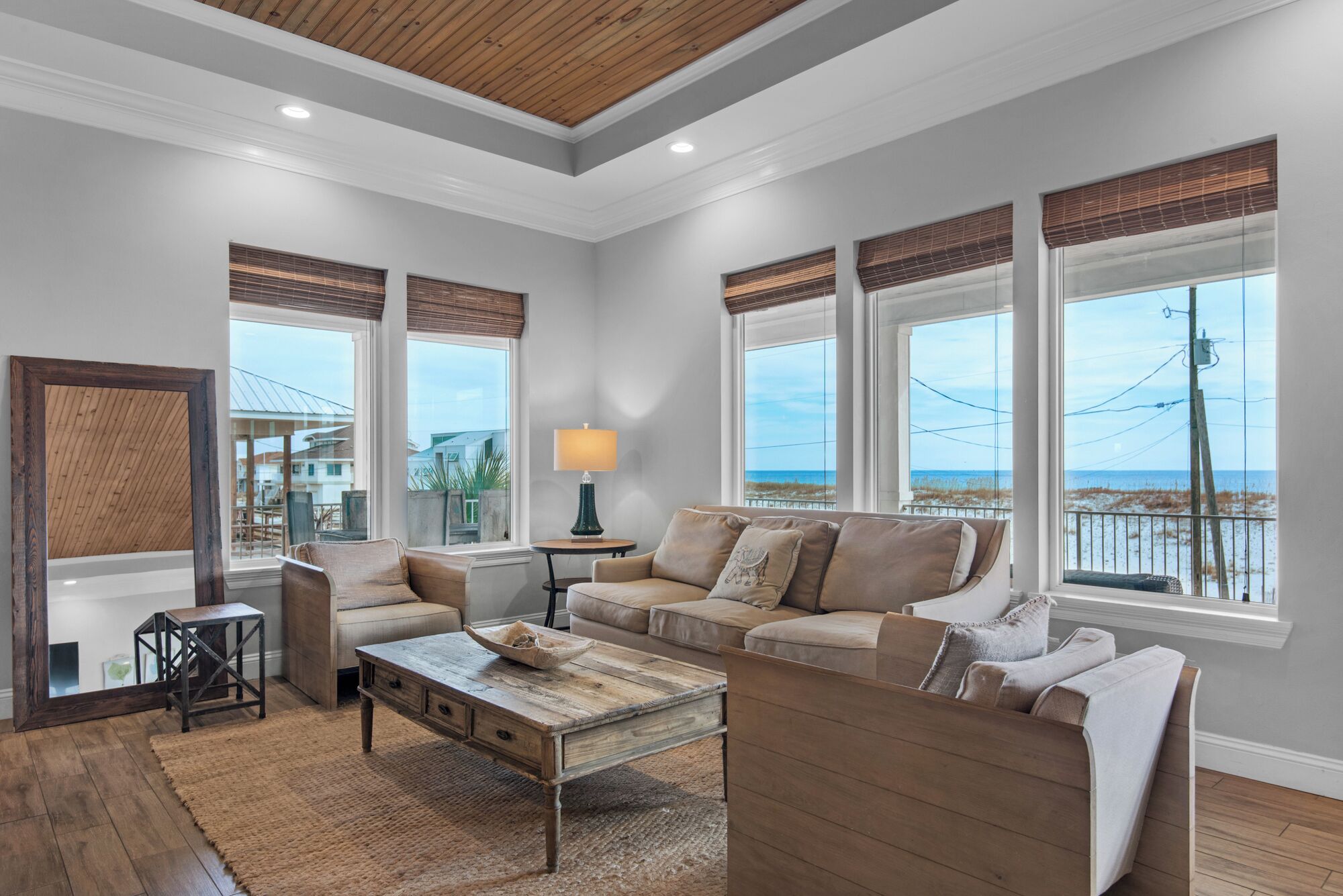 A spacious living room with a large window overlooking a beach, a wooden ceiling, and a cozy seating area.