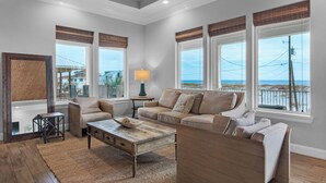 A spacious living room with a large window overlooking a beach, a wooden ceiling, and a cozy seating area. - 🌊 The Great Escape | Sleeps 22 w/ Gulf Views, Private Pool, + Crow's Nest 🏖️ (Pensacola Beach)