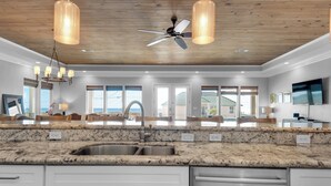 A modern kitchen with granite countertops, stainless steel appliances, and a large window overlooking a beach. - 🌊 The Great Escape | Sleeps 22 w/ Gulf Views, Private Pool, + Crow's Nest 🏖️ (Pensacola Beach)