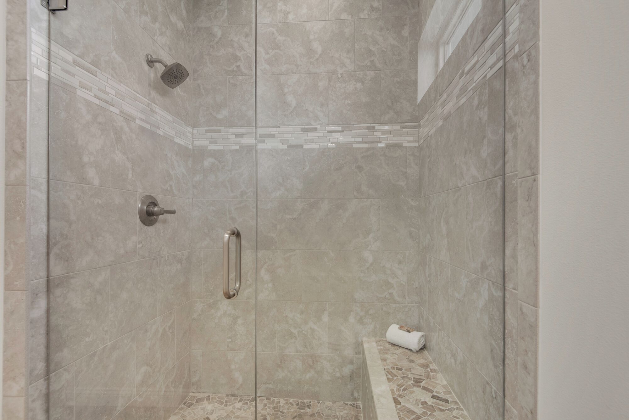 Une douche à l’italienne avec une porte en verre, un pommeau de douche amovible, un porte-serviettes et un sol carrelé.