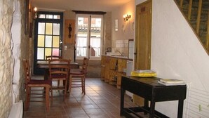 Una habitación rústica con una mesa y sillas de madera, una zona de cocina con fregadero y una escalera que sube a un nivel superior.