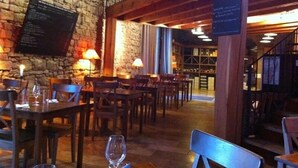 Un restaurante con paredes de piedra, mesas y sillas de madera. Hay un menú en la pared y un cartel con información.
