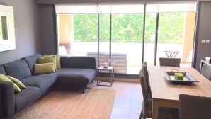 Una sala moderna con un sofá seccional gris oscuro, una mesa de comedor de madera y vistas a un área exterior a través de grandes puertas correderas de vidrio.