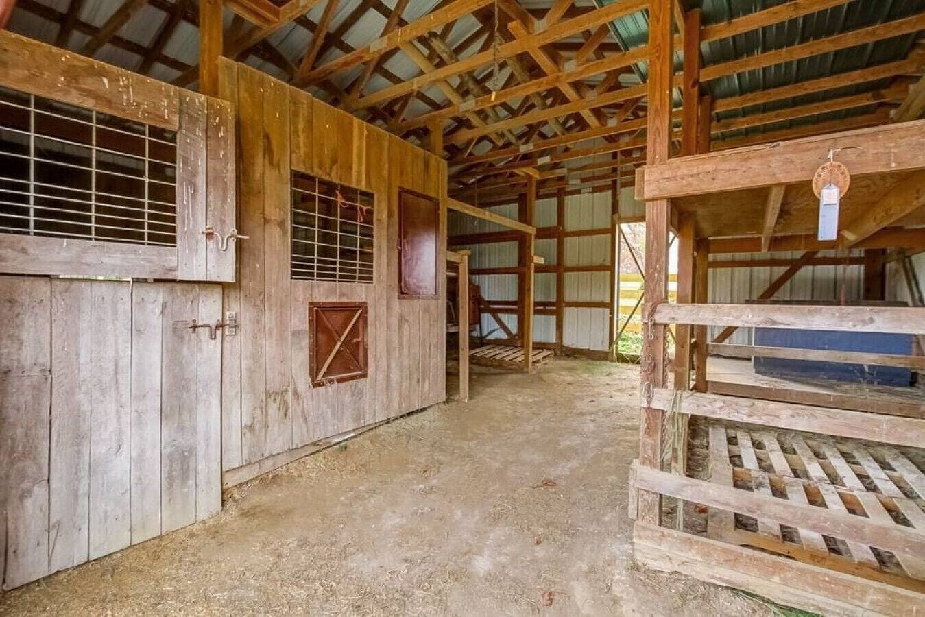 A rustic barn interior with wooden walls, metal-framed windows, and a dirt floor.
