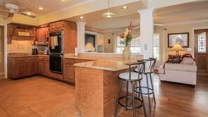 A spacious kitchen with wooden cabinets, a central island with stools, and a dining area with a sofa and table. - Private 3 Acre Home North Nashville (Goodlettsville)