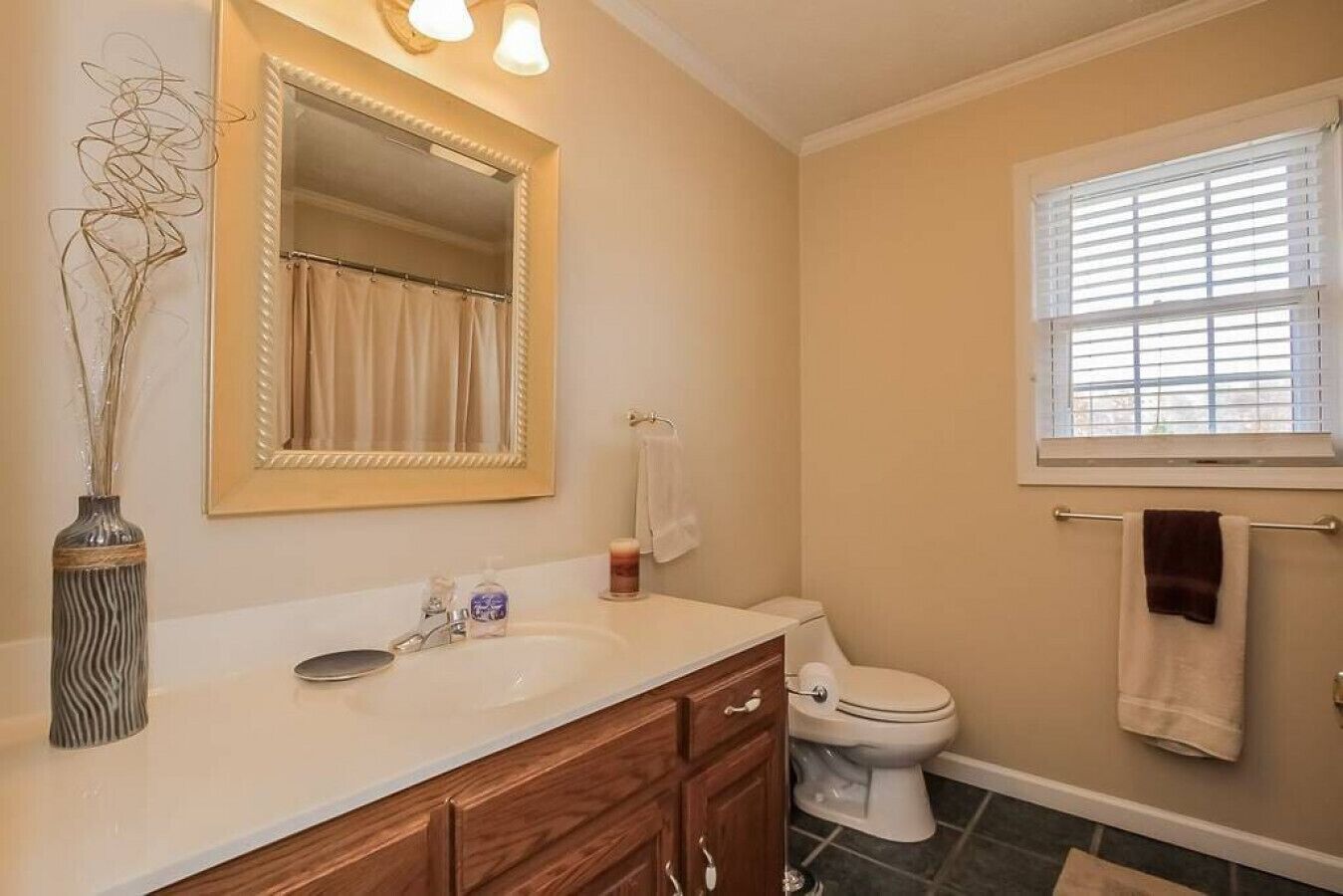 A bathroom with a vanity, a toilet, a window with blinds, and a mirror.