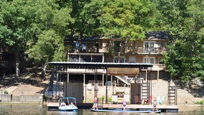 A lakeside property with a dock, a covered seating area, and a building with a balcony. - Family Friendly Lake Home, Private Boat Dock, Lake Ozark  (Lake Ozark)