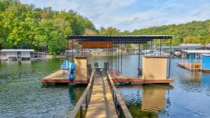 A wooden dock leading to a covered seating area with a view of a lake and docked boats. - Family Friendly Lake Home, Private Boat Dock, Lake Ozark  (Lake Ozark)