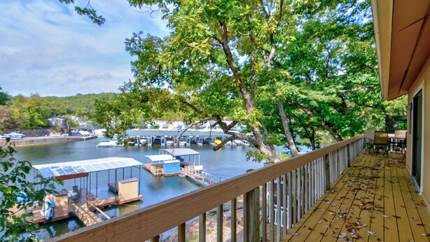 A wooden deck overlooking a marina with boats docked, a covered area with seating, and a view of the water and hills in the background. - Family Friendly Lake Home, Private Boat Dock, Lake Ozark  (Lake Ozark)