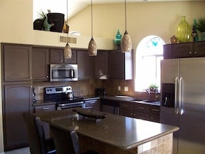 Une cuisine moderne avec des meubles de couleur sombre, des appareils en acier inoxydable et des luminaires suspendus.