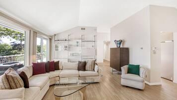 A modern living room with a sectional sofa, a glass coffee table, and a small armchair. There is a built-in shelving unit with decorative items and a dark cabinet.