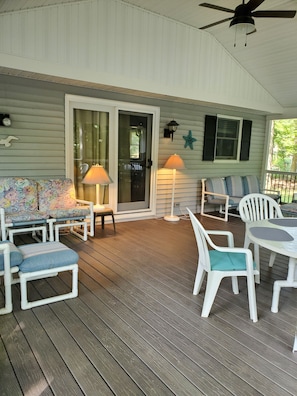 A covered porch with wooden flooring, white furniture, and two table lamps.