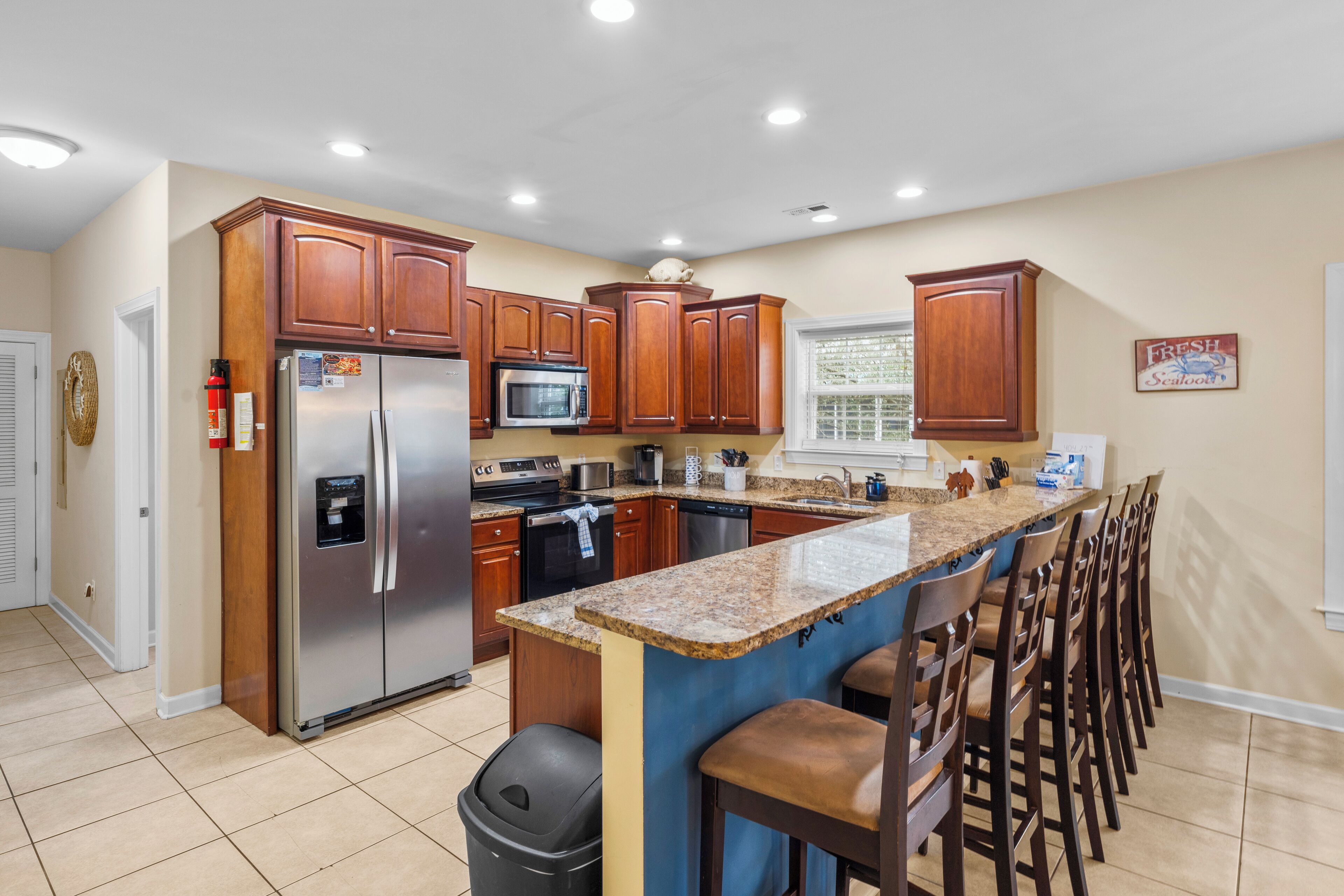 A modern kitchen with wooden cabinets, stainless steel appliances, a granite countertop, and a bar area with stools.