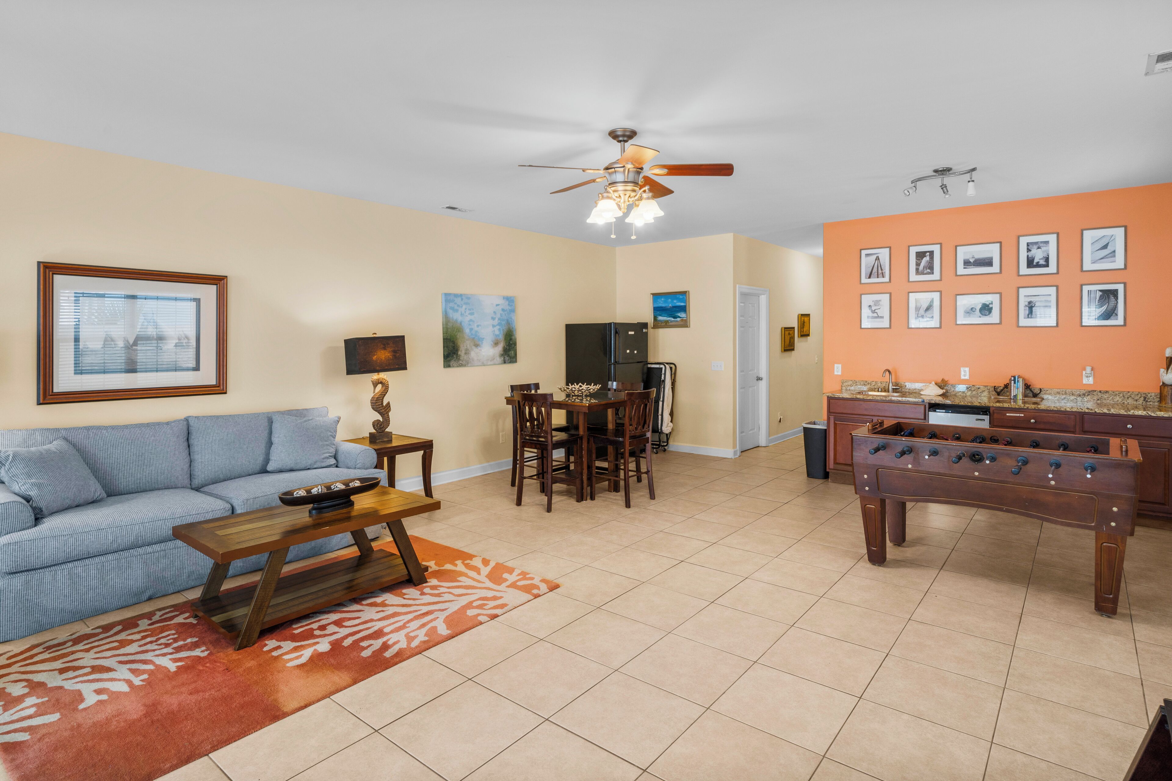 A living room with a sofa, coffee table, dining table, and chairs. There is a kitchen area with a refrigerator, stove, and sink.