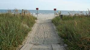Un sentiero sabbioso con tavole di legno, circondato da erba alta, che conduce verso l'oceano.