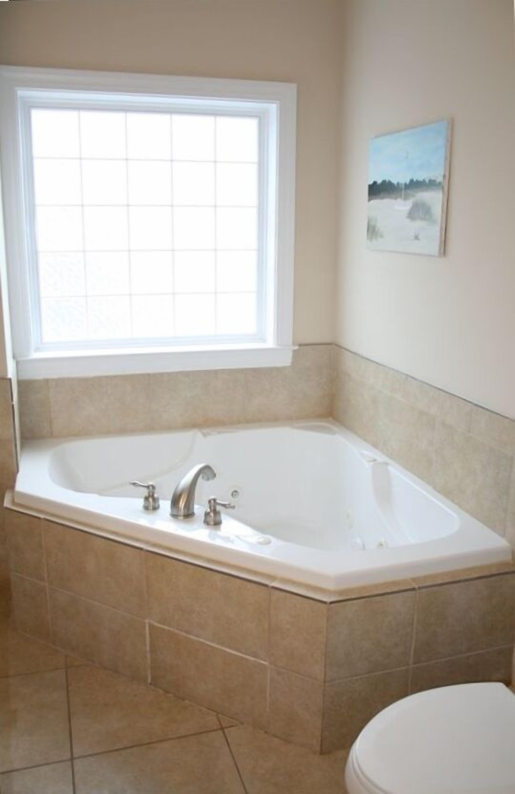 A bathroom with a large bathtub, a window, and a painting on the wall.