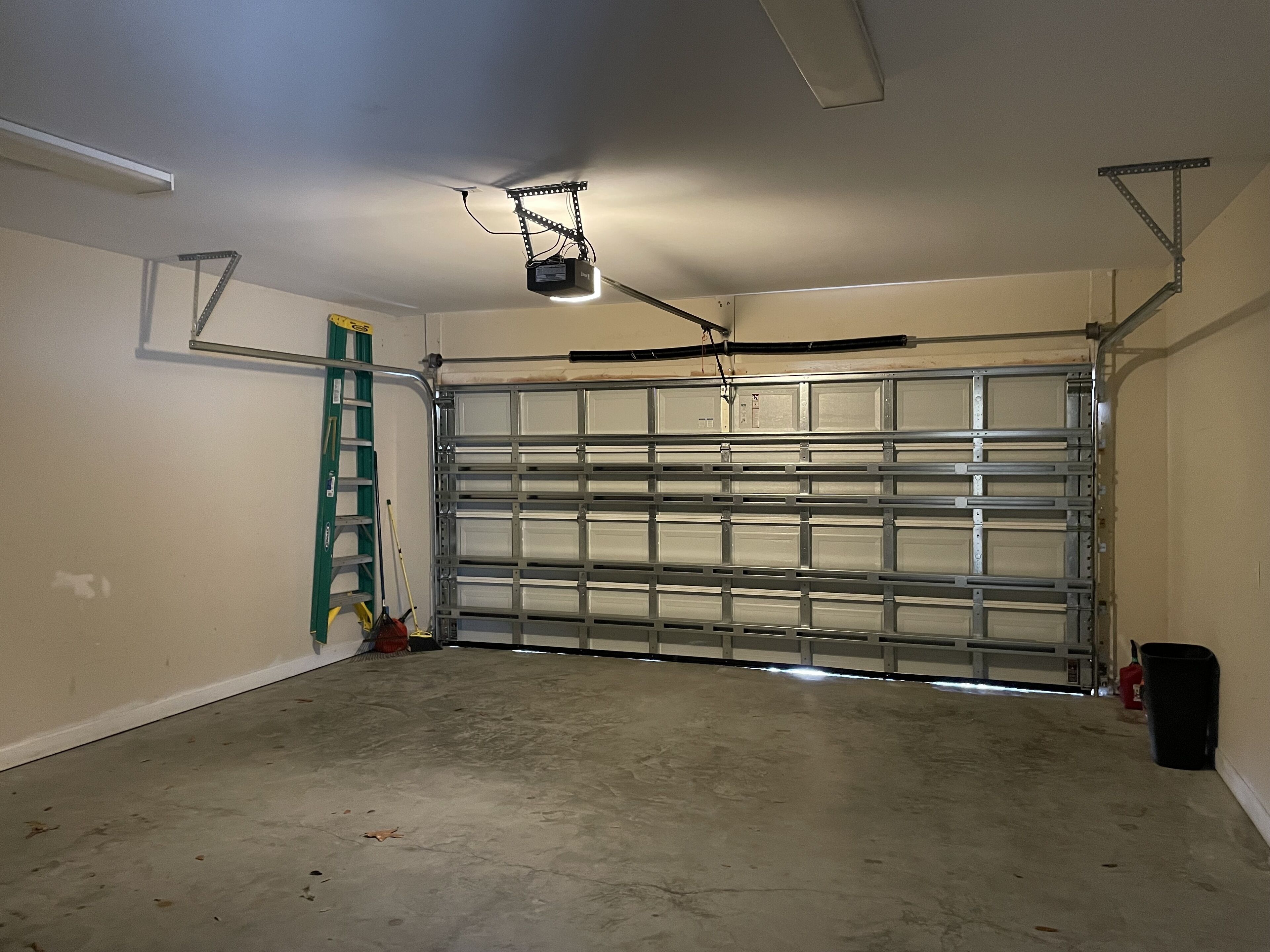 A garage with a metal door, a ceiling fan, and a ladder leaning against the wall.