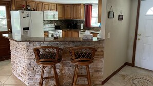 A kitchen with wooden cabinets, a granite countertop, a built-in island with two bar stools, a refrigerator, a microwave, and a stove. - Bass Fishing, Kayaking or just Relaxing From Your Own Private Home & Boat Dock  (Dunnellon)