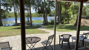 A patio with a table and chairs overlooking a lake, surrounded by trees and a dock. - Bass Fishing, Kayaking or just Relaxing From Your Own Private Home & Boat Dock  (Dunnellon)
