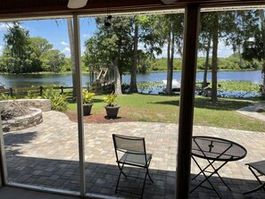 Un patio con vista a un lago, muebles de exterior y una terraza de madera con escaleras que bajan a un muelle.