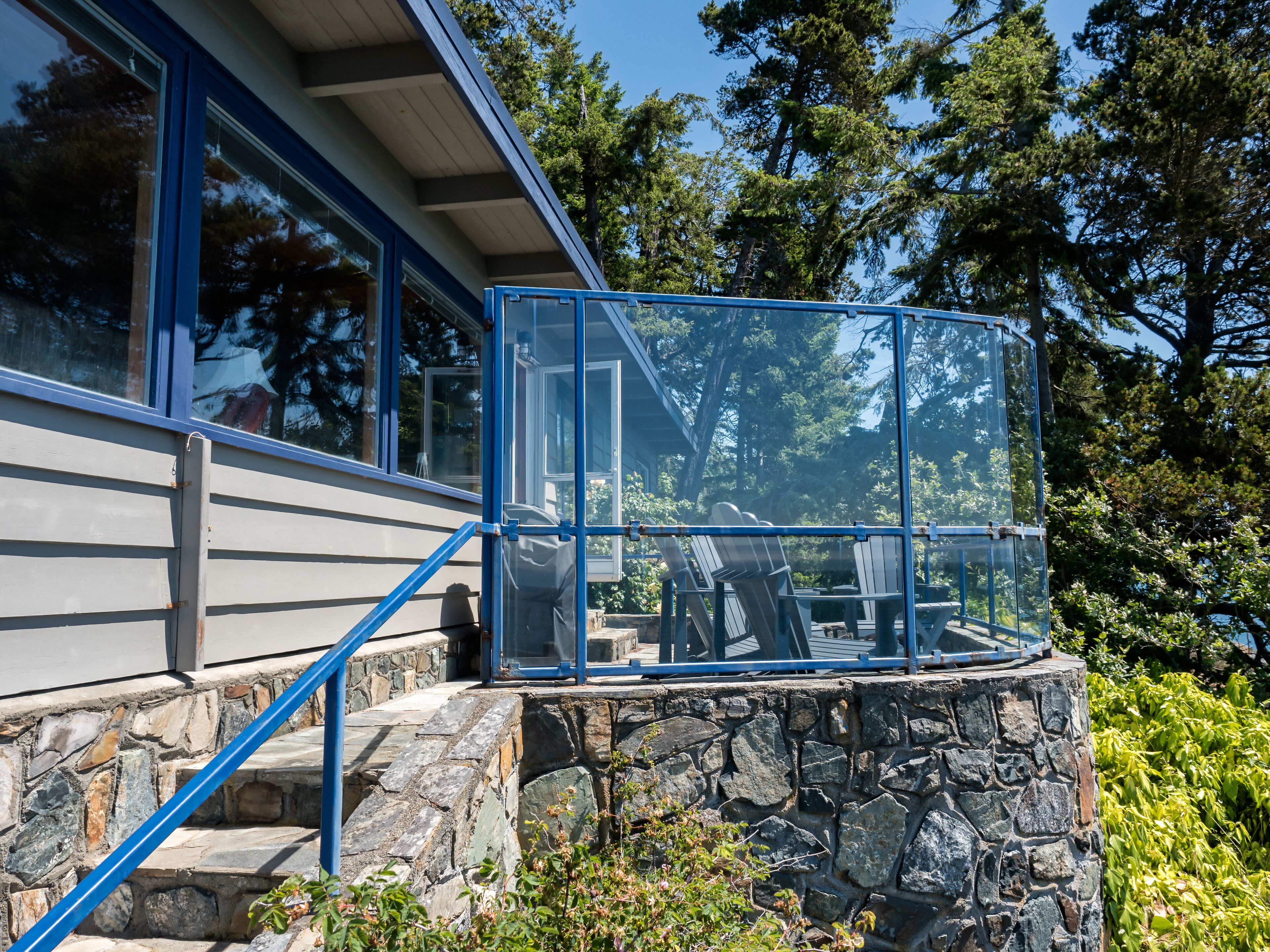 Una casa moderna con una escalera de piedra que conduce a un porche con paredes de vidrio y mobiliario exterior.