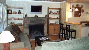 Ein gemütliches Wohnzimmer mit Kamin, einem darüber montierten Fernseher und einem Essbereich mit Bar.