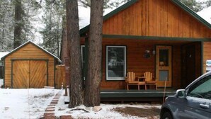 Eine Holzhütte mit Veranda, Garage und einem davor parkenden Auto.