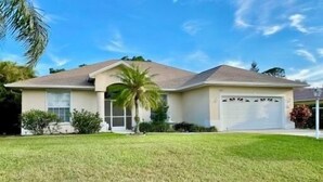A single-story house with a garage, a front lawn, and a palm tree. - Peaceful Florida Retreat...Spacious 3BR/3BA Private Pool Home (Bonita Springs)