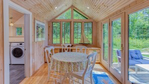 Un intérieur de chalet chaleureux avec un coin repas, de grandes fenêtres et une vue sur la forêt.