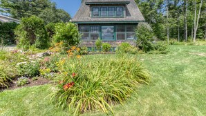 Une maison avec un cadre de fenêtre vert, un toit en pente et un jardin où poussent différentes plantes et fleurs.