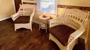 A room with two wicker chairs, a small table, a clock on the wall, and a window with blinds. - Moosewood Cottage - Hot Tub, Downtown, Dog Friendly (Moab)