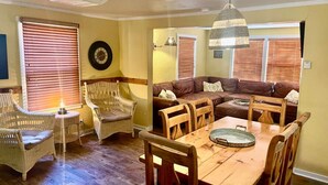 A cozy living room with a wooden dining table, wicker chairs, a brown leather sofa, and a hanging light fixture. - Moosewood Cottage - Hot Tub, Downtown, Dog Friendly (Moab)