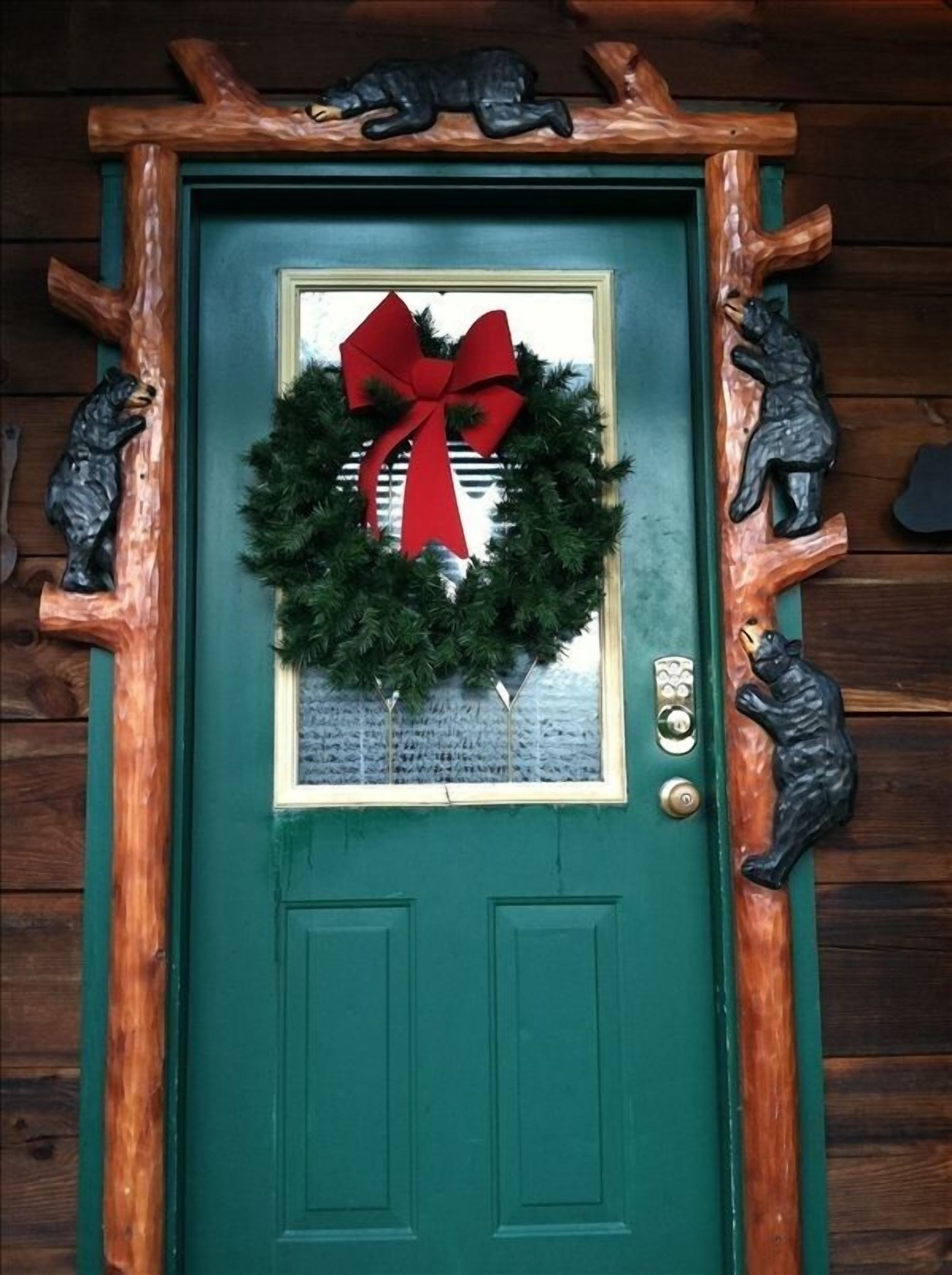A green door with a wreath and red bow, flanked by bear sculptures.