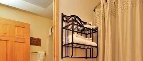 A bathroom with a sink, toilet, and a mirror. There is a towel rack above the toilet and a shower curtain.