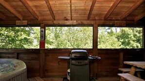 A wooden cabin with a hot tub, a grill, and picnic tables.