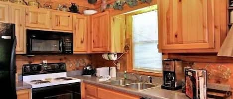 A wooden cabin-style kitchen with a stove, microwave, sink, and various appliances.