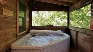 A wooden cabin with a hot tub and a window overlooking a forest.