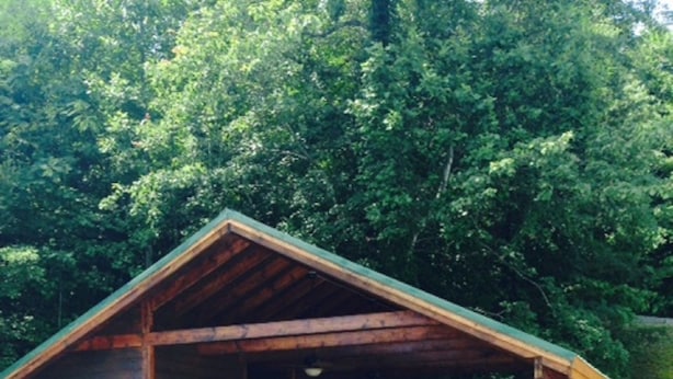 A wooden cabin with a porch, surrounded by dense trees.