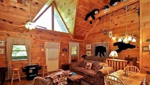 A cozy cabin interior with a wooden ceiling, a sofa, a dining table, and a fireplace.