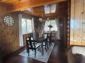 A wooden interior with a dining table, chairs, a clock, and a window with curtains. - Pet &. Family Treehouse style cabin in woods- Come Experience Fall (Julian)