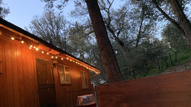 A wooden cabin with string lights, a fire pit, and a glass of red wine on a bench. - Pet &. Family Treehouse style cabin in woods- Full Time Rental as of Oct 1 (Julian)