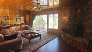 A wooden interior with a stone fireplace, a sofa, a coffee table, and a ceiling fan. - Pet &. Family Treehouse style cabin in woods- Full Time Rental as of Oct 1 (Julian)