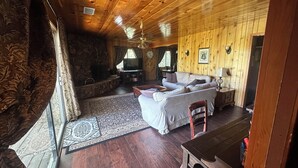A wooden interior with a sofa, a TV, a dining table, and a stone wall. - Pet &. Family Treehouse style cabin in woods- Full Time Rental as of Oct 1 (Julian)