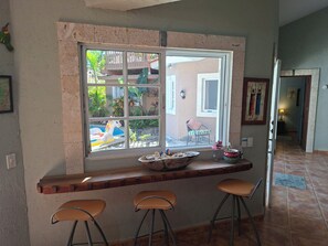 A kitchen with a window overlooking a balcony, a wooden bar counter with stools, and a potted plant on the counter.